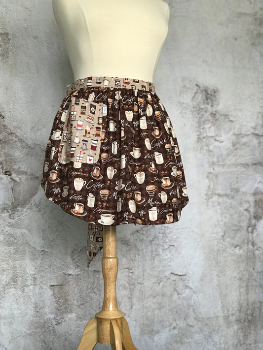 Elsie’s Diva Apron is a double-sided kitchen apron featuring generously sized pockets, 100% high quality cotton fabric, and long waist ties to make this apron well suited for most figures. Coffee cups and coffee quotes adorn this fun apron.