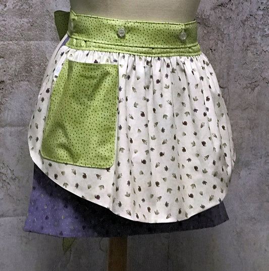 Ida’s Diva Apron is a patent pending convertible kitchen apron that can be worn 8 different ways by using the buttons on the waistband to flip, add or subtract both the apron front and back. Featuring generously sized pockets, 100% high quality cotton fabric, and long waist ties to make this apron well suited for most figures. With tiny flowers of lavenders and pinks and strawberry blossoms highlighted by a waistband of soft green teensy dots, this apron is a happy helper in any setting.