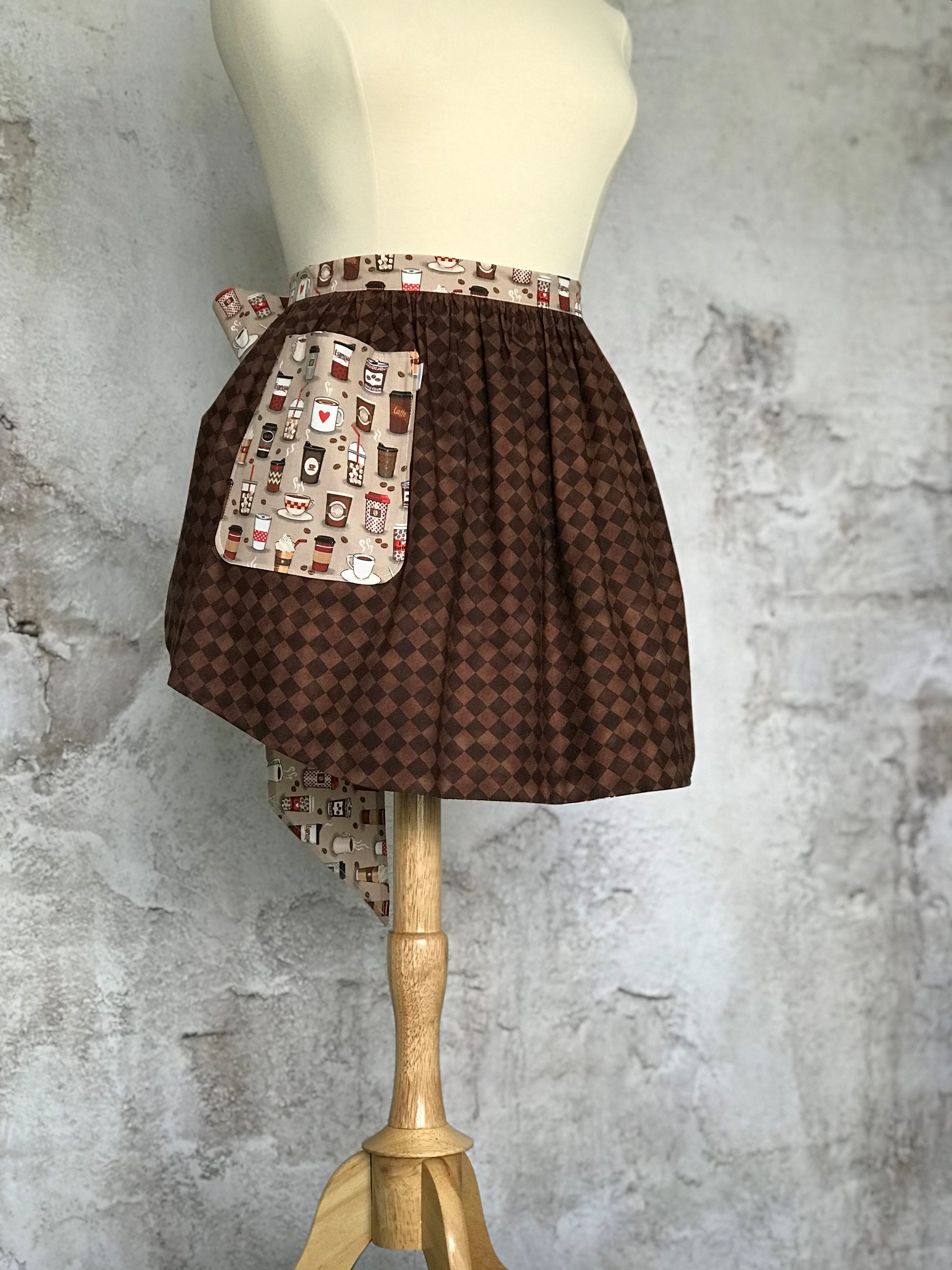 Elsie’s Diva Apron is a double-sided kitchen apron featuring generously sized pockets, 100% high quality cotton fabric, and long waist ties to make this apron well suited for most figures. Coffee cups and coffee quotes adorn this fun apron.